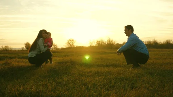 ママとパパ夕日で芝生の上子供と一緒に再生します。家族の幸せの概念。赤ちゃんは、お母さんにお父さんから芝生の上行きます。子が公園での最初のステップを取る. — ストック写真