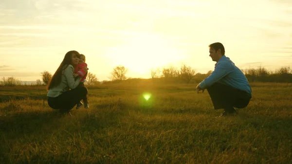 Máma s tátou hrají s klukem na trávě při západu slunce. koncepce rodinné štěstí. dítě jde na trávníku od táty k mámě. dítě bere první kroky v parku. — Stock fotografie