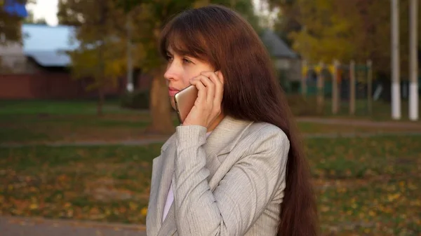 Девушка разговаривает по мобильному телефону и несет черный портфель в руке в парке вечером . — стоковое фото