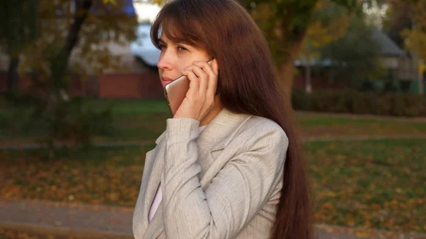 Девушка разговаривает по мобильному телефону и несет черный портфель в руке в парке вечером . — стоковое фото