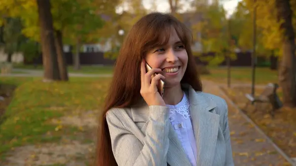 Мобильный телефон прогуливаясь по осеннему парку и улыбаясь — стоковое фото