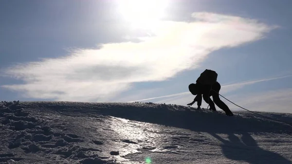 チームワークを獲得する欲望。ロープの上の登山者は、丘の頂上に登る友人を助けます。冬の太陽の明るい光の丘の上の方のシルエット。スポーツ観光の概念. — ストック写真