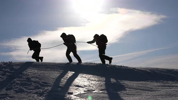 Командное желание победить. Альпинисты на веревке помогают другу подняться на вершину холма. Силуэт путешественников зимой на холме в ярких лучах солнца. концепция спортивного туризма . — стоковое фото