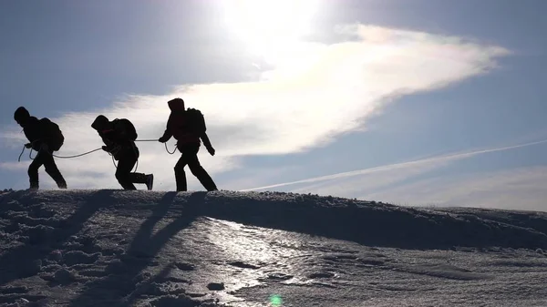 Týmová práce touha vyhrát. Horolezci na laně pomoci příteli vyšplhat až na vrchol kopce. Silueta cestujících v zimě na kopci v zářivé paprsky slunce. koncepce cestovního ruchu, sportu. — Stock fotografie