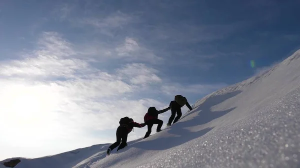 ekip çalışması kazanmak arzusu. Dağcılar derajat birbirlerinin ellerini karlı bir dağ tepesine tırmanmak bir arkadaşa yardım etmem. parlak güneş ışınlarının bir tepe üzerinde yolcuları kışın. spor turizmi kavramı.