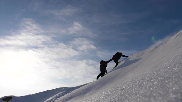 Командное желание победить. Альпинисты срывают друг с друга руки, чтобы помочь другу подняться на вершину снежной горы. Путешественники зимой на холме в ярких лучах солнца. концепция спортивного туризма . — стоковое фото