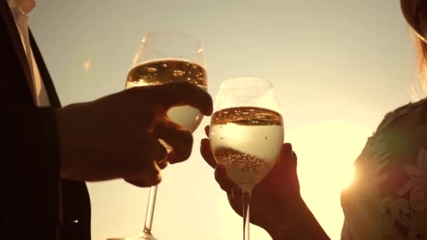 Champagne sparkles and foams in sun. couple in love holding wine glasses with sparkling wine on background of sunset. closeup. teamwork of loving couple. celebrating success and victory. Slow motion — Stock Video