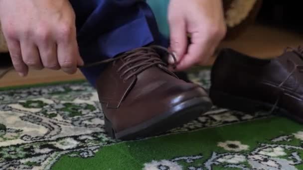 Uomo allacciatura lacci delle scarpe su scarpe marroni, un uomo in camicia bianca e pantaloni scuri. L'uomo d'affari si veste al mattino per lavorare . — Video Stock