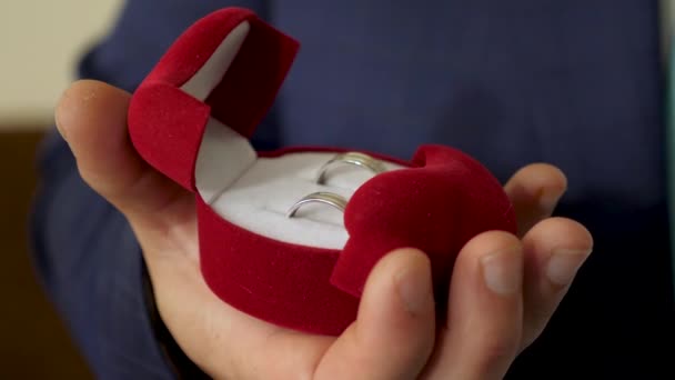 El novio sostiene la caja con anillos de boda en su mano para su propuesta a su amada. Crear una nueva familia. Primer plano — Vídeos de Stock