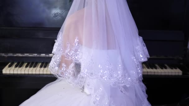 Meisje in een witte jurk bespeelt de piano. De bruid voert een stukje muziek op de piano. muziekbusiness. — Stockvideo