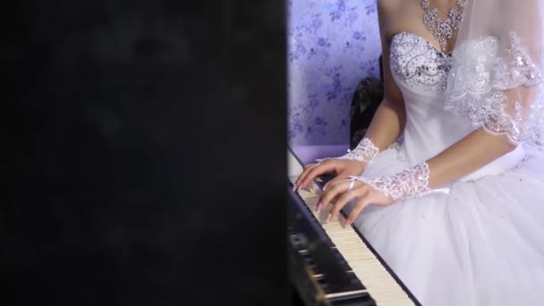 Mãos de uma jovem tocando o instrumento teclado clave. menina em um vestido branco tocando para o piano preto. A noiva executa uma peça de música no piano. negócio da música . — Vídeo de Stock