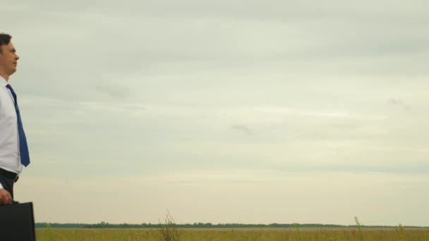 Landbouwingenieur gaat over het veld. Close-up. zakenman in wit overhemd in blauwe band met zwarte aktetas doorloopt park voor een belangrijke vergadering. — Stockvideo