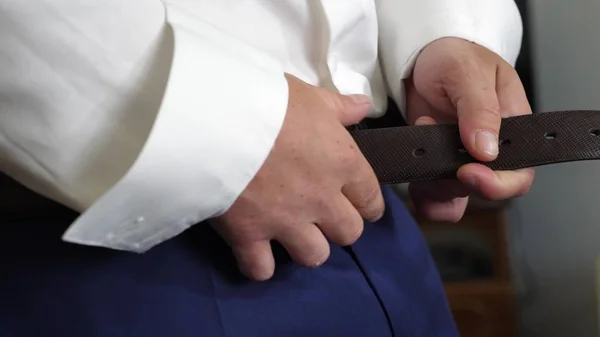 Man in een wit overhemd zet gordel op zijn broek. Close-up. de mens krijgt gekleed voor werk in de ochtend. — Stockfoto