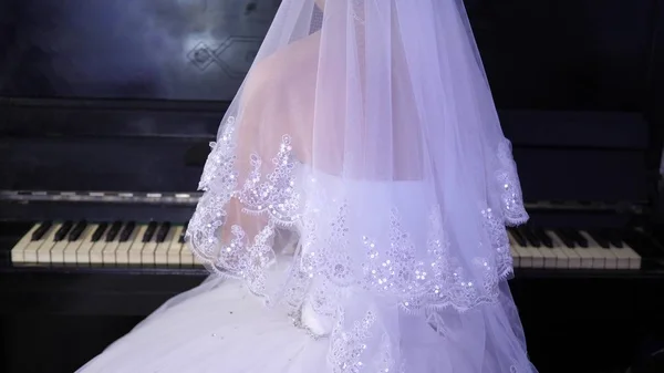 Chica con un vestido blanco toca el piano. La novia interpreta una pieza musical en el piano. negocio de música . — Foto de Stock