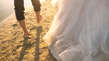 yalınayak damat ve gelin Beyaz giysili bir plajda Nehri boyunca yürümek. aşık çift suya yakın yaz aylarında kumsalda yürür. yakın çekim. Ağır çekim. mutlu aile kavramı.