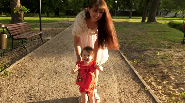 Child learns to walk along path in park in summer, mother walks with the baby — Stock Photo, Image