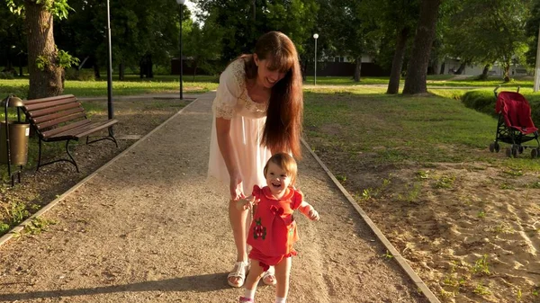 Ребенок учится ходить по дорожке в парке летом, мать гуляет с ребенком — стоковое фото