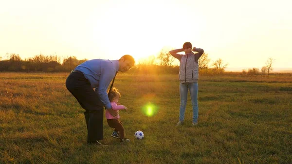 Familie spielt mit jüngerem Baby mit Fußball im Park bei Sonnenuntergang. glücklicher Vater und Kind kicken Ball. Glückliches Familienkonzept. Zeitlupe — Stockfoto