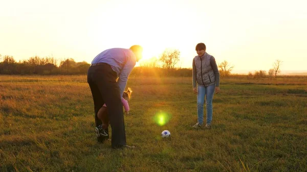 Rodina hrát s mladším dítětem s fotbalovým míčem v parku při západu slunce. Šťastný otec a dítě kopnout míč. šťastný rodinný koncept. Zpomalený pohyb — Stock fotografie