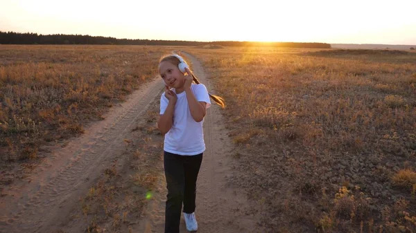 Sport joggen bij zonsondergang buiten stad doen. jong meisje in een witte T-shirt treinen bij zonsondergang en luistert naar muziek met koptelefoon. — Stockfoto