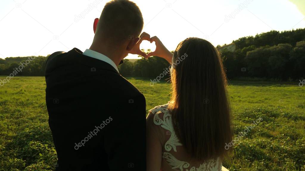 girl and her boyfriend making a heart shape by the hands opposite a beautiful sunset on the horizon. sun is in the hands. teamwork of a loving couple. celebrating success and victory.