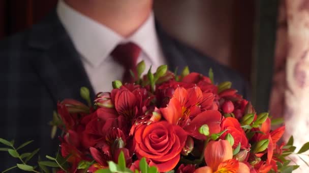 Beau bouquet de fleurs dans les mains d'un homme à la mode pour la femme qu'il aime. Gros plan. beau bouquet de roses rouges dans les mains des hommes en veste en cravate rouge et chemise blanche. gros plan — Video