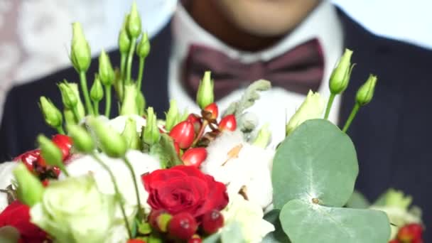 Vacker bukett vita rosor och röda blommor i händerna på mannen i jacka i röd fluga och vit skjorta. Närbild. Vacker bukett blommor i händerna på en fashionabel man för kvinnan han älskar. — Stockvideo