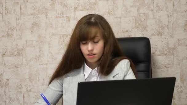 Bilgisayarda çevrimiçi iş görüşmesi. Kız bilgisayarda ofiste sandalyede oturan ve defter notları alır. Laptop arkasında çalışan genç kadın girişimci. Sekreter defter yazıyor. — Stok video