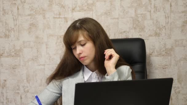 Young female entrepreneur working behind laptop. online business conversation on computer. girl sitting in chair in office at computer and takes notes in notebook. secretary writes pen in notebook — Stock Video