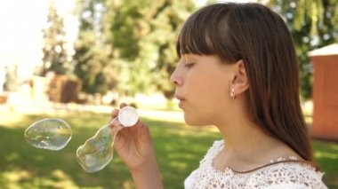 mutlu kız parkta Bahar, yaz ve gülümseyen güzel sabun köpüğü üfleme. Ağır çekim. Genç Kız parkta şehrin içinden seyahat.