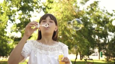 Genç Kız parkta oynarken ve kabarcıklar objektife içine üfleme. Ağır çekim. İlkbahar, yaz ve gülümseyen içinde parkta sabun köpüğü üfleme güzel kız.