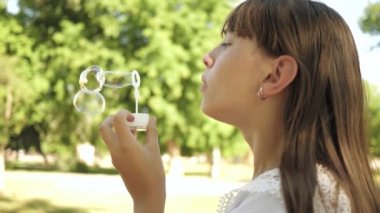 Genç Kız parkta oynarken ve kabarcıklar yakın çekim üfleme. Ağır çekim. İlkbahar, yaz ve gülümseyen içinde parkta sabun köpüğü üfleme güzel kız.