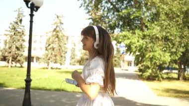 neşeli kız baharında yazında park gider. Seninle seyahat etmek gitmek dans, elini sallayarak ve çağıran güzel kız. Müzik, kızla telefonunda kulaklık, gülümseyen.
