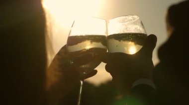Şampanya parıldıyor ve güneşte köpükler. İki aşık ile köpüklü şarap şarap gözlük günbatımı arka plan üzerinde tutarak. portre. seven çift, takım çalışması. başarı ve zafer kutluyor. Ağır çekim