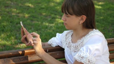 bir akıllı telefon kullanan güzel kız güzel bir yeşil parkta bir bankta bir mektup yazıyor. Ağır çekim. Bin yıllık kadında genç jestleri ekranın üzerinde yapma Botanik Bahçesi,.