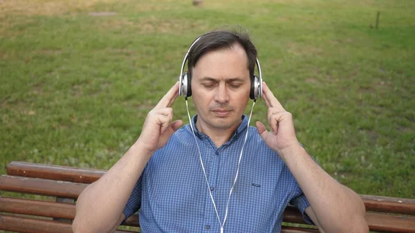 Jovem bonito descansando em um parque ouvindo música de seu smartphone com fones de ouvido e dançando fora em um parque em um banco no centro da Europa . — Fotografia de Stock