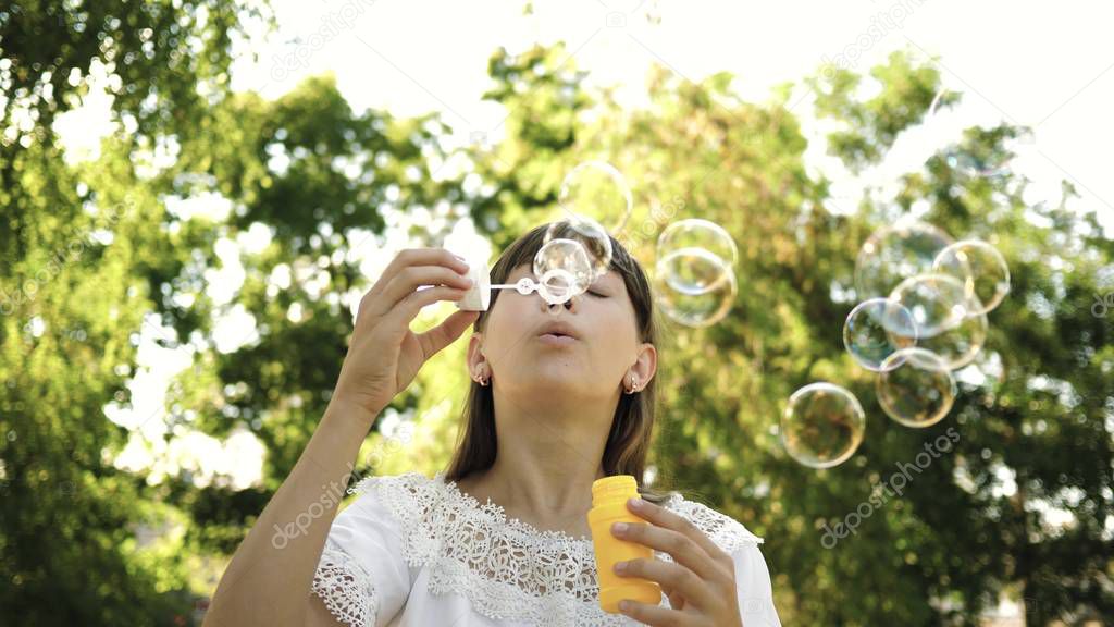 young girl playing in the park and blowing bubbles into the camera lens. Slow motion. Beautiful girl blowing soap bubbles in the park in spring, summer and smiling.