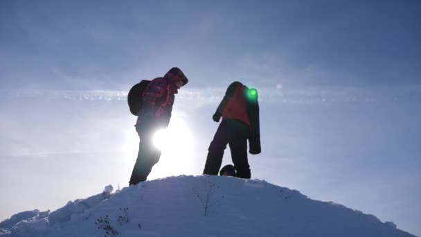 Tres turistas con mochilas en invierno subieron la colina en los rayos del sol brillante. Los escaladores en la cima de una montaña nevada se regocijan en su éxito. Viajeros de trabajo en equipo. concepto de estilo de vida deportivo — Vídeo de stock