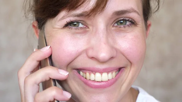 Chica hablando en un teléfono celular se ríe, dientes primer plano. mujer hablando en el teléfono inteligente y sonriendo de cerca. necesidad de cepillarse los dientes . — Foto de Stock