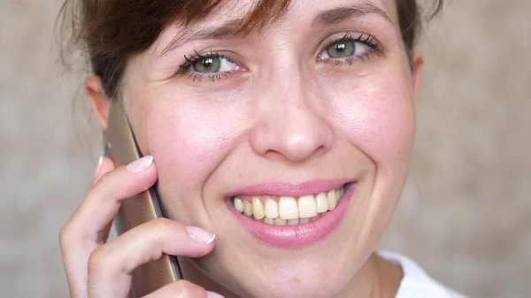 Chica hablando en un teléfono celular se ríe, dientes primer plano. mujer hablando en el teléfono inteligente y sonriendo de cerca. necesidad de cepillarse los dientes . — Foto de Stock