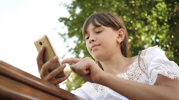 快乐的女孩使用智能手机翻转网页在互联网上的公园在长凳上。特写。在植物园的年轻的千年妇女, 在手机上做手势显示. — 图库照片