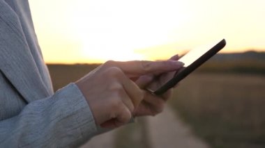 kızın parmak dokunmatik ekran tablet, smartphone. yakın çekim. Eller bir tablet tutarak ve e-postaları parkta günbatımında kontrol. Kızlar el bir mobil ileti smartphone ekranında yazdırır..