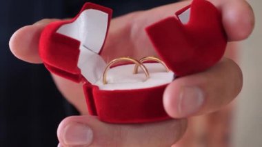 Damat altın alyanslarla dolu kutusunu elinde tutuyor. Yakın plan. Altın hediye madalyası. Sevgilisi için mücevherler.