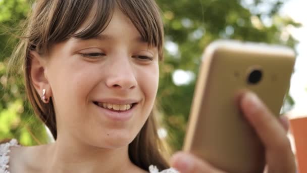 公園のベンチでは、インターネット上のページをめくってスマート フォンを使用して幸せな女の子。クローズ アップ。電話のディスプレイ上のジェスチャーを作り、樹木園の若い千年女性. — ストック動画