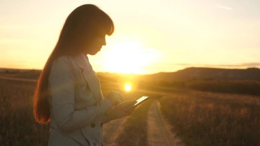 Eller bir tablet tutarak ve e-postaları parkta günbatımında kontrol. kızın parmak dokunmatik ekran tablet, smartphone... Kızlar el bir mobil ileti smartphone ekranında yazdırır..