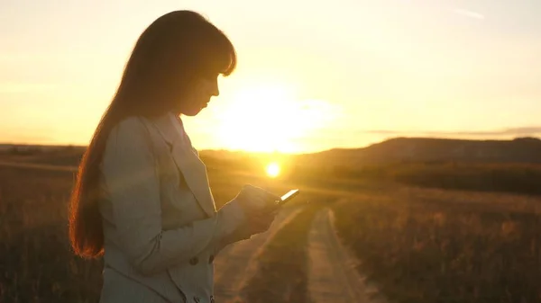 Les mains des femmes tiennent une tablette et vérifient les courriels dans le parc au coucher du soleil. doigts de fille écran tactile de la tablette, smartphone.. les filles impriment à la main un message mobile sur l'écran du smartphone . — Photo