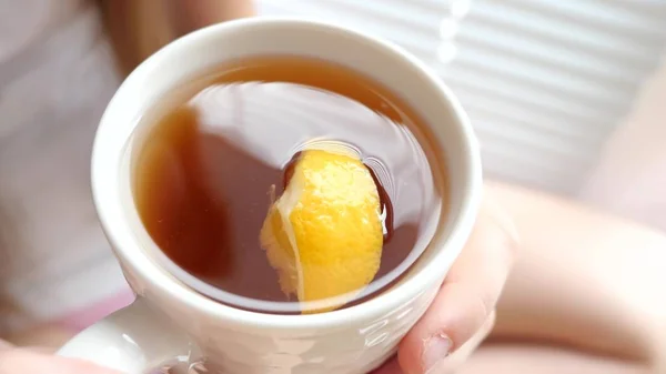 Красивая девушка пьет из кружки горячий чай с лимоном глядя в окно . — стоковое фото