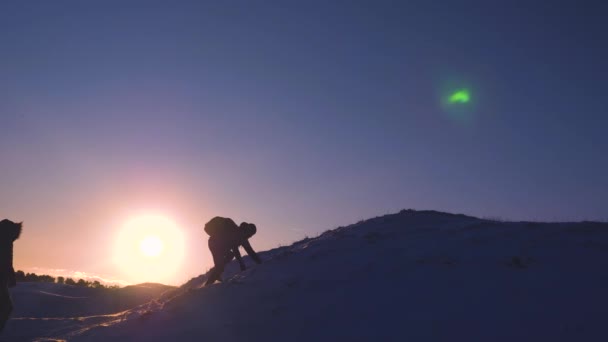 Klimmers op een besneeuwde berg in hun succes verheugen, hun handen te verhogen en gelukkig springen. sport toerisme concept. toeristen met rugzakken helpen elkaar te klimmen van de top van de heuvel in heldere stralen van de zon. — Stockvideo