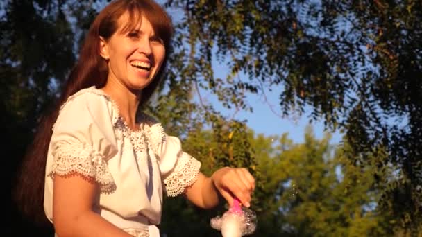 Mujer sopla grandes burbujas de jabón y se ríe mientras camina en el parque. Paseos de verano y juegos en la naturaleza — Vídeo de stock
