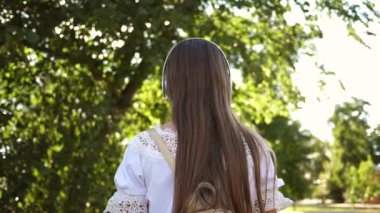 Bir şehir ile müzik ve gülümseyen kulaklıklar sokak turist kız. genç kız şehrin sokaklarında seyahat. Ağır çekim. Uzun saçlı bir kız şehir etrafında seyahat.